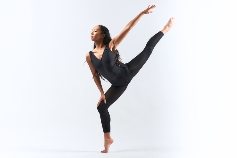 Pre-Professional dancer in black uni-tard shownin center of white background, on arms and one leg outstretched behind